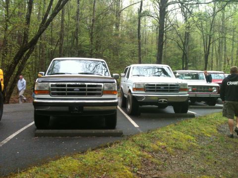 1992 Ford Bronco - Two Ford Broncos are parked in a lot surrounded by trees. The vehicle on the left appears to be a 1992 model.
