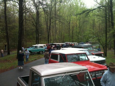 1992 Ford Bronco - A gathering of Ford Broncos and a pickup truck are parked in a wooded area, likely at an event or meet-up.
