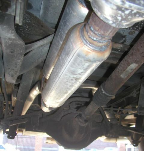 1988 Ford Bronco - Underside view of a vehicle's exhaust system showing a polished stainless steel muffler or resonator connected to darker exhaust piping, mo…