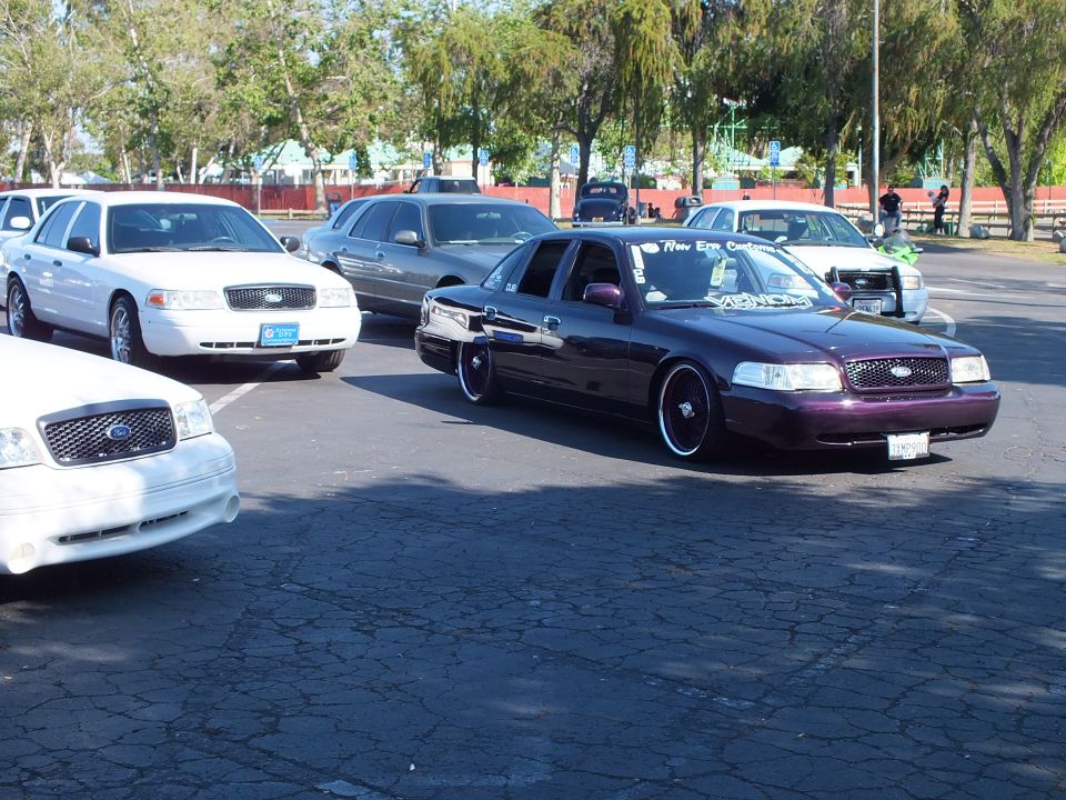 Lowered dark purple Ford Crown Victoria sedan and white sedans in a paved lot