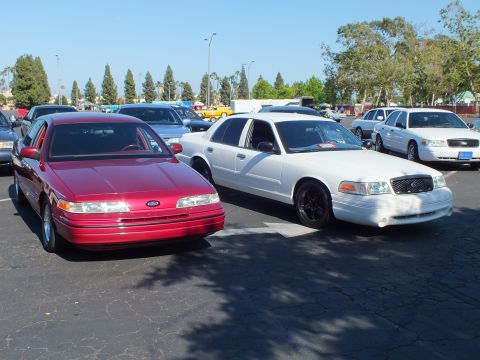 Red Ford Taurus sedan parked beside a white Ford Crown Victoria in a lot