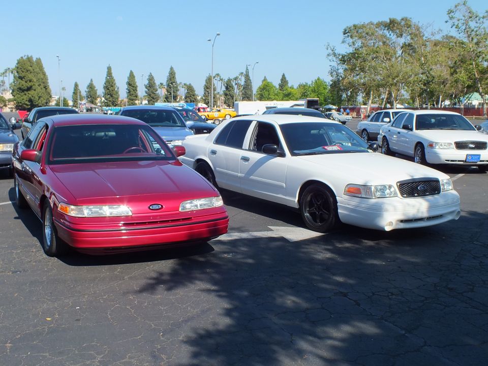 Red Ford Taurus sedan parked beside a white Ford Crown Victoria in a lot