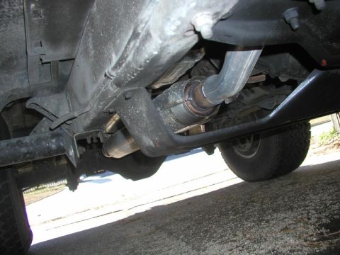 1988 Ford Bronco - Underbody view along the passenger side of a lifted truck showing the exhaust routing: a catalytic converter and welded pipe running back o…
