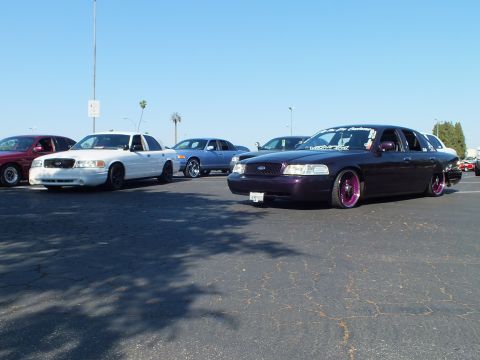 Purple bagged Ford Crown Victoria laid out on purple-lip wheels at a parking lot car meet
