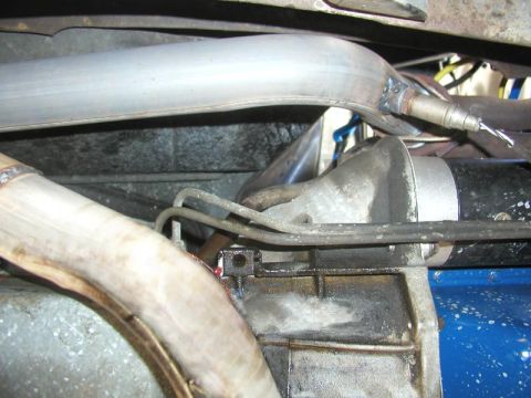 1988 Ford Bronco - Underside view of exhaust and drivetrain components, showing bare metal exhaust header pipes, a driveshaft, transmission housing, and metal…