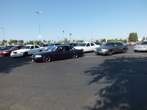 Lowered dark purple sedan and white cars across a wide parking lot