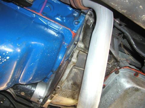 1988 Ford Bronco - Underhood view looking down alongside a blue-painted engine with an orange-sealed pan rail, where a polished stainless exhaust pipe curves…