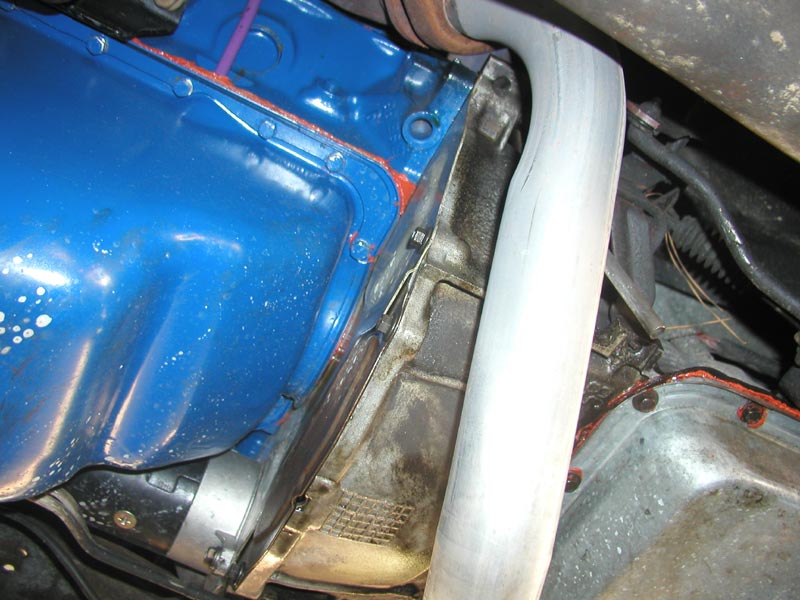 Polished exhaust pipe routed past a blue engine block seen from underneath