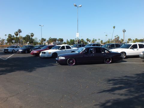 Maroon slammed sedan on pink wheels in a sunlit parking lot
