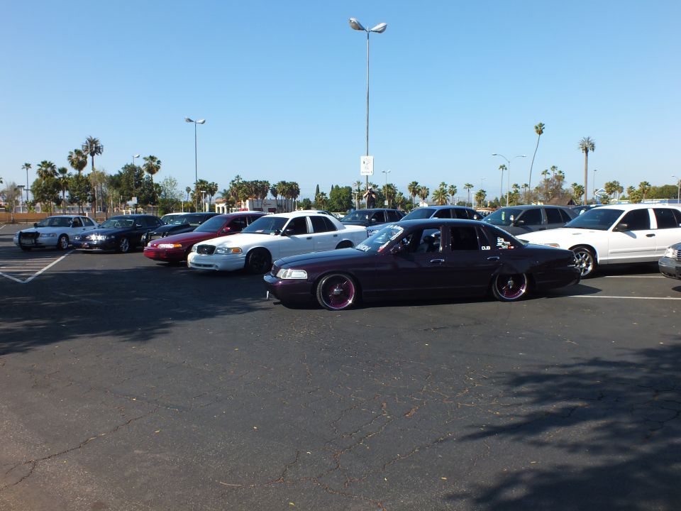 Maroon slammed sedan on pink wheels in a sunlit parking lot