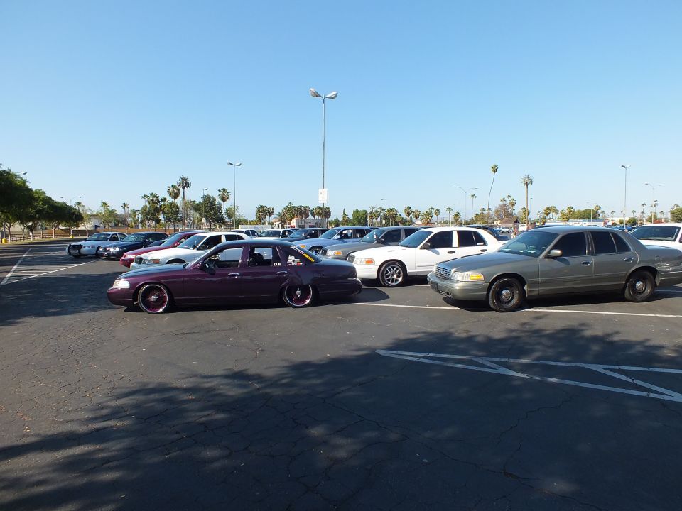 Maroon slammed sedan and tan sedan among parked cars in a large lot