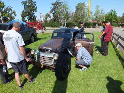 2003 Ford Crown Victoria - bare-metal Ford rat rod pickup with a checkered roof sits on grass at a car show as several men look it over.