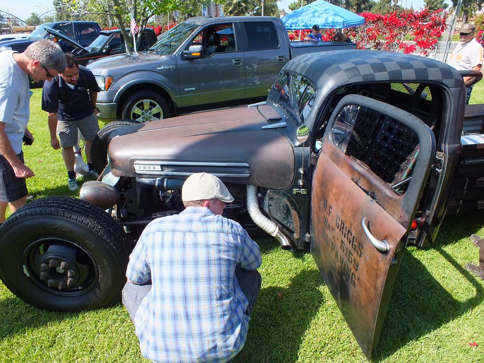 Front of a Ford rat rod truck with open door and man crouching