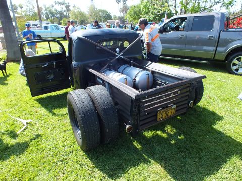 2003 Ford Crown Victoria - rear of a black Ford rat rod truck shows a FORD-stamped tailgate, yellow plate, and dual rear wheels on grass.