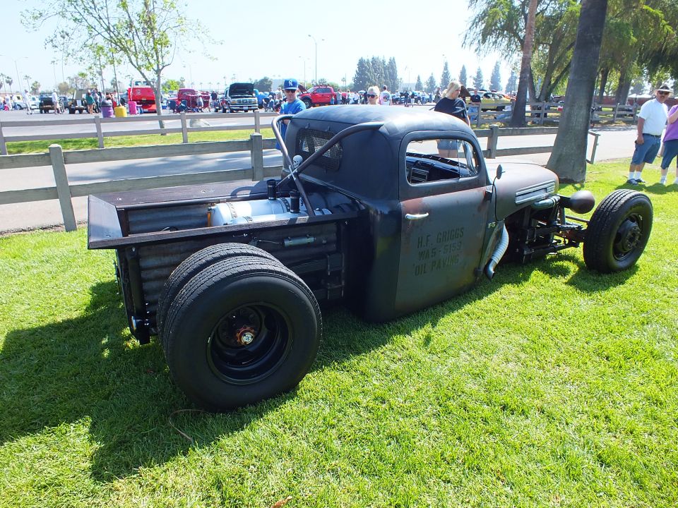 Side view of a black Ford rat rod truck on grass at a car show