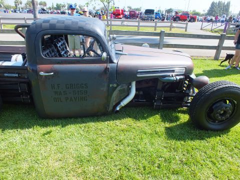 2003 Ford Crown Victoria - chopped Ford F-5 rat rod truck shows hand-painted 'H.F. Griggs Oil Paving' lettering and a side-exit exhaust on grass.