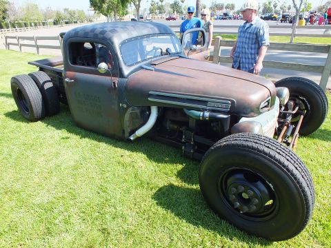 2003 Ford Crown Victoria - low Ford F-5 rat rod truck with side-exit exhaust and black steel wheels sits on grass as two men watch.