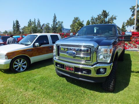 2003 Ford Crown Victoria - lifted Ford Super Duty pickup with a chrome FORD grille parks beside a white woody-trim Ford Excursion SUV on grass.