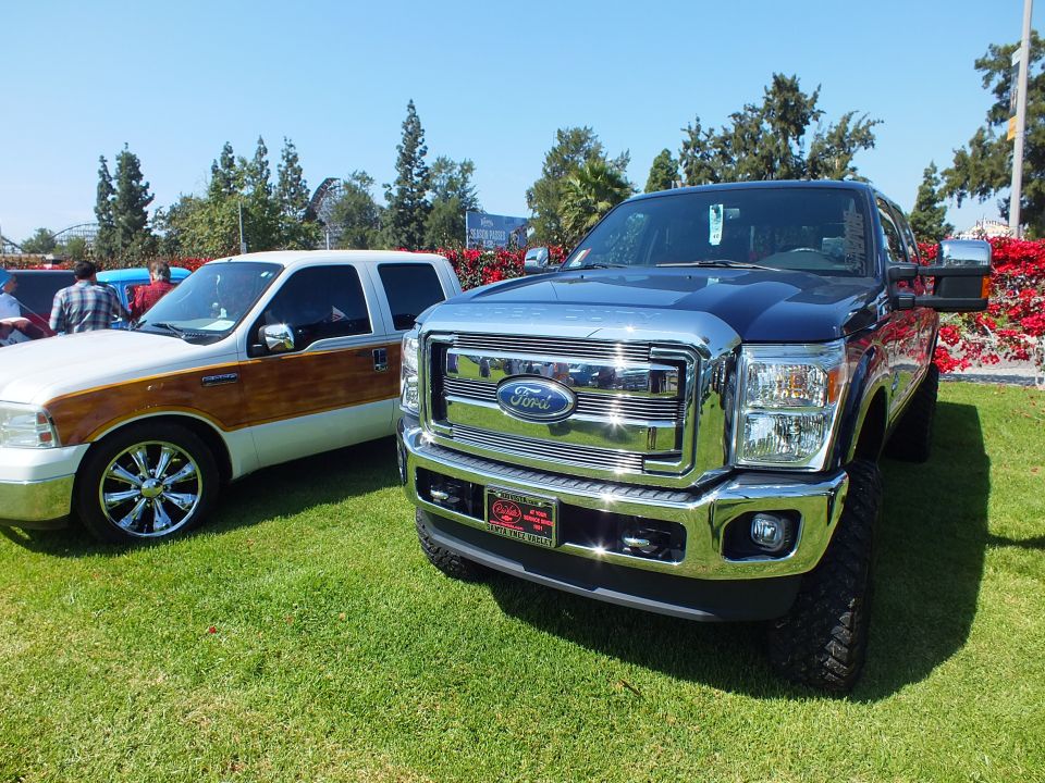 Lifted Ford Super Duty with chrome grille beside a woody-trim Excursion