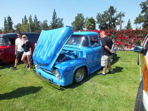 2003 Ford Crown Victoria - light-blue classic Ford pickup with darker flame paint and an open hood sits on grass as spectators look it over at a car show.