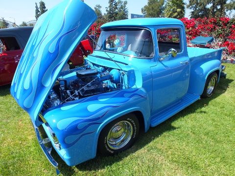 2003 Ford Crown Victoria - light-blue classic Ford pickup with flame graphics and open hood reveals a chrome-dressed V8 engine at an outdoor show.