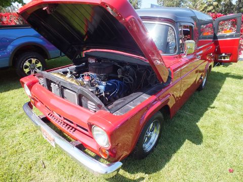 2003 Ford Crown Victoria - dark-red classic pickup with open hood displays its engine and chrome wheels on a grassy show field beside other trucks.