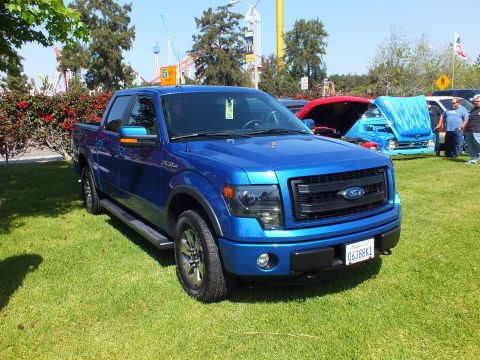 2003 Ford Crown Victoria - Front three-quarter of a blue Ford F-150 FX4 crew-cab pickup on grass, with carnival rides and other show vehicles behind.