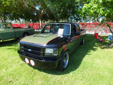 2003 Ford Crown Victoria - black lowered Ford crew-cab pickup with a gold-and-red hood stripe and black wheels sits on grass with a show placard inside.