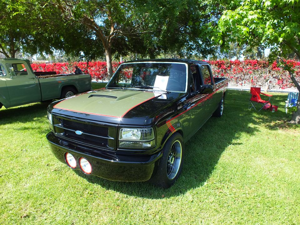 Black lowered Ford crew-cab pickup with gold hood stripe and black wheels