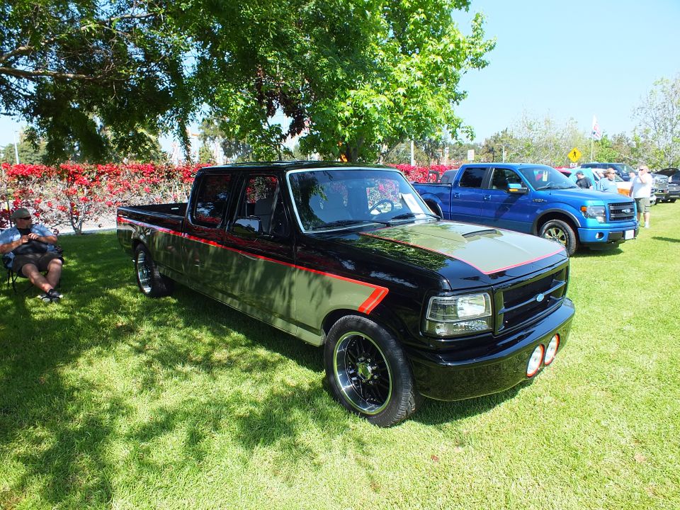 Black lowered Ford crew-cab pickup with red stripe, blue F-150 in background