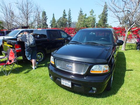 2003 Ford Crown Victoria - glossy black Ford pickup with chrome grille sits front-and-center on a lawn while a man stands at a second black truck behind it.