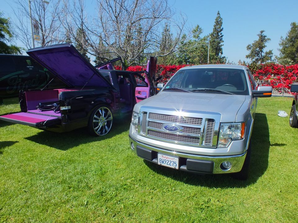Silver Ford F-150 pickup beside purple custom truck with open lambo door on grass