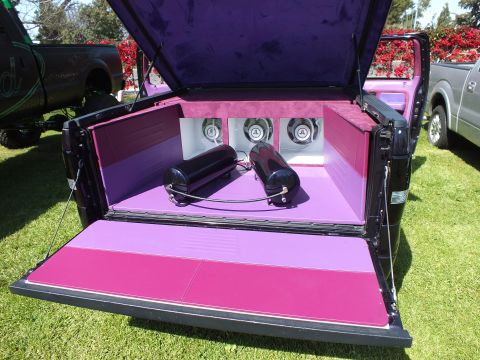 2003 Ford Crown Victoria - custom truck bed lined in pink and purple houses three round subwoofer speakers and twin cylindrical canisters under a velvet lid.