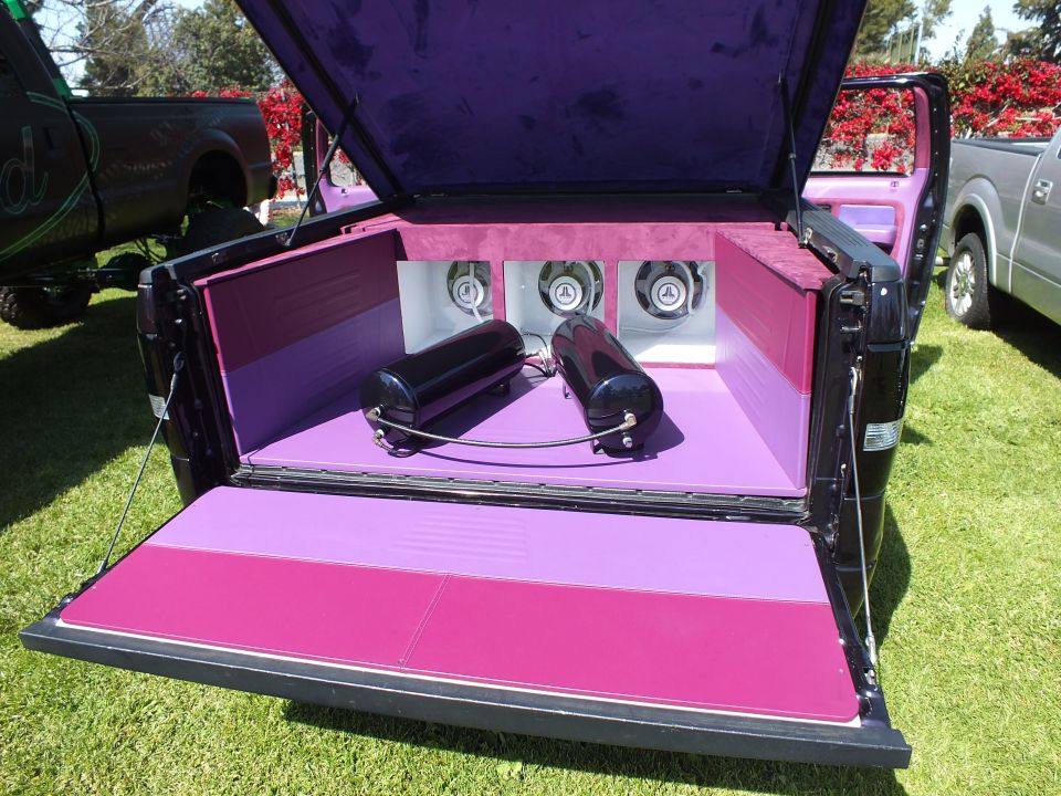 Close-up of custom truck bed lined in pink and purple with three speaker subwoofers