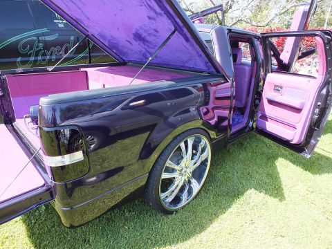 2003 Ford Crown Victoria - lowered black custom truck on large chrome wheels sits with its door open, exposing a pink-and-purple custom interior.