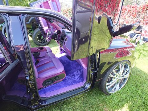 2003 Ford Crown Victoria - custom truck's open suicide doors expose a pink-and-purple cabin, with a glossy black body panel reflecting the show field.