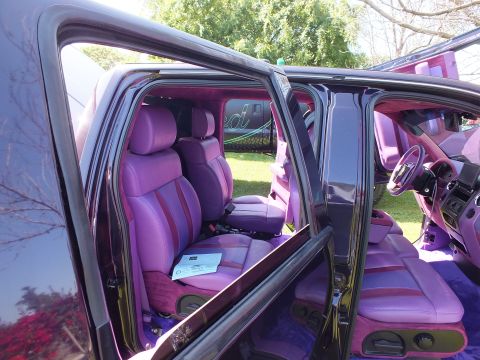 2003 Ford Crown Victoria - Both rows of a custom truck cabin are upholstered in purple and magenta leather, seen through wide-open suicide doors.