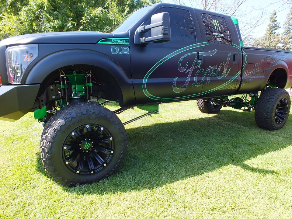 Side of lifted matte-black Ford truck with green Ford script and DUB graphics on grass