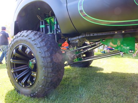 2003 Ford Crown Victoria - front suspension of a lifted truck shows green-painted control arms and steering links above a large mud-terrain tire.