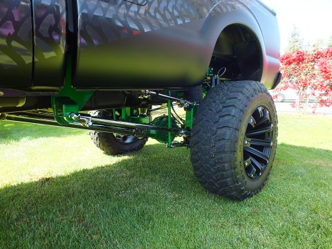 2003 Ford Crown Victoria - rear underside of a lifted truck reveals green-painted suspension links and a black off-road wheel with mud-terrain tire.