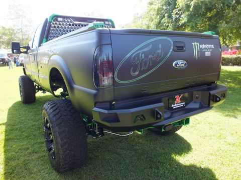 2003 Ford Crown Victoria - rear of a matte-black lifted Ford Super Duty shows a teal Ford oval, Monster Energy badge and a steel off-road bumper.