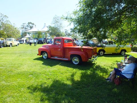 2003 Ford Crown Victoria - bright red vintage Ford pickup sits on a grassy show field with spectators, tents and other classic cars in the background.