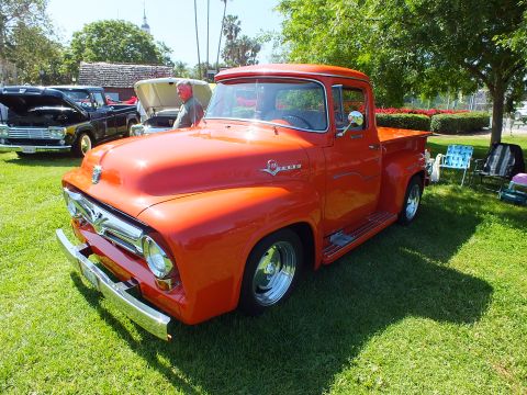 2003 Ford Crown Victoria - bright orange restored 1950s Ford pickup truck displayed on a grassy lawn at a sunny outdoor car show.