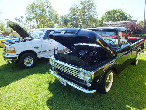 2003 Ford Crown Victoria - black restored vintage pickup with whitewall tires and open hood parked next to a white Ford pickup at an outdoor show.