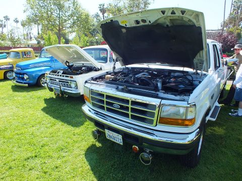 2003 Ford Crown Victoria - white Ford pickup displayed with its hood open revealing the engine, lined up with other trucks on a grassy show field.