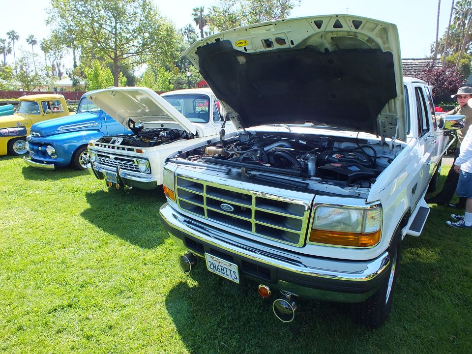 White Ford pickup with open hood showing engine at a car show
