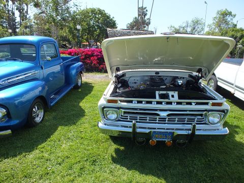2003 Ford Crown Victoria - white Mercury pickup with its hood up sits on grass beside a blue restored vintage Ford pickup at a car show.