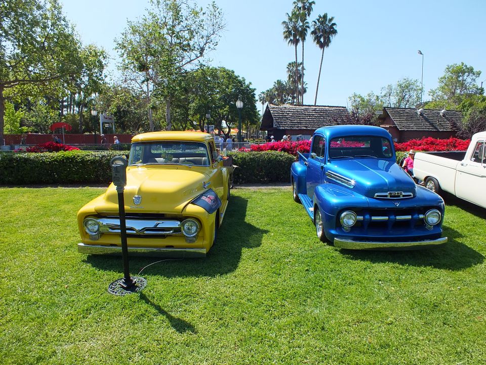Yellow and blue vintage Ford pickups parked side by side on grass