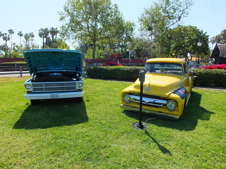 Teal pickup with open hood beside a yellow vintage Ford pickup on grass