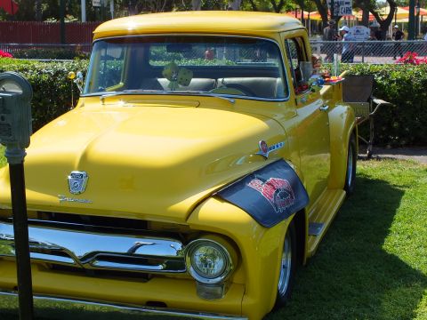 2003 Ford Crown Victoria - glossy yellow vintage Ford pickup with a lowered stance and an airbrushed mural on the fender, parked at a street car show.